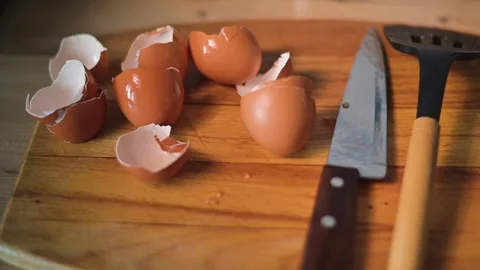 Eggshells are scattered on a wooden cutting board next to several uncracked eggs 動画素材 344667572