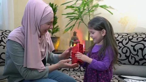 Eid al-Adha gift box. Happy Muslim mother in hijab gives her daughter a gift for Stock Footage 156433510