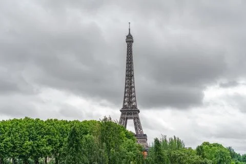 The Eiffel Tower emerging over trees with stormy clouds Fotos Stock