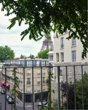Eiffel Tower view through leafy tree branches and Paris street buildings Stock Photos