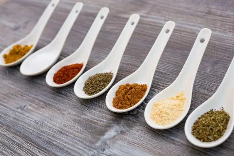 Eight ceramic spoons lined up in a line filled with colorful spices on artifi Stock Photos