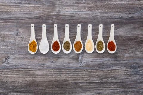 Eight ceramic spoons lined up in a line filled with colorful spices on artifi Stock Photos