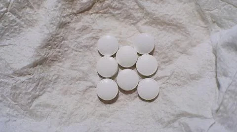 Eight white tablets lying on a crumpled gray-white napkin Stock Photos
