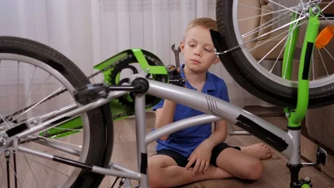 An eight-year-old boy repairs a bicycle at home with a wrench. Stock Footage 305293306