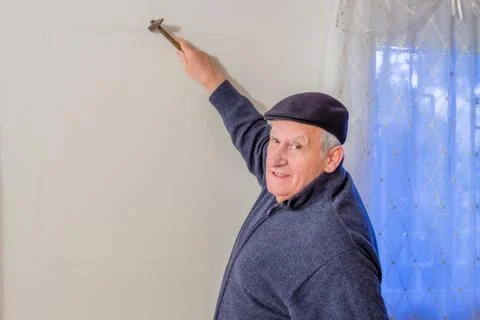 Eighty-year-old man holding hammer against wall Stock Photos