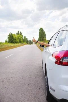 Ein junges Mädchen, das ein Auto fährt, streckt ihre Hand aus dem Fenster . Stock Photos