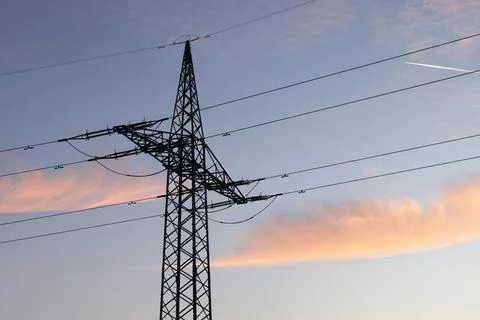  Ein Strommast mit Stromleitung steht im Abendlicht auf einem Feld. (Theme... Foto stock