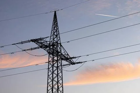  Ein Strommast mit Stromleitung steht im Abendlicht auf einem Feld. (Theme... Foto stock
