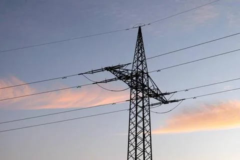  Ein Strommast mit Stromleitung steht im Abendlicht auf einem Feld. (Theme... Foto stock