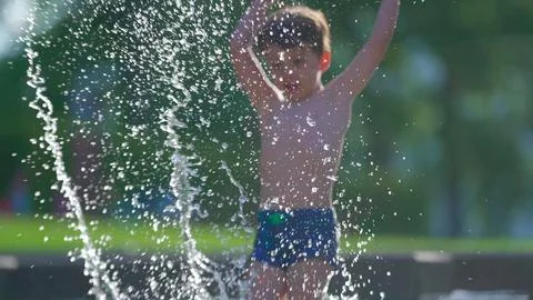Elated child sending water jets skyward in pool on summer afternoon, small .. Stock Photos
