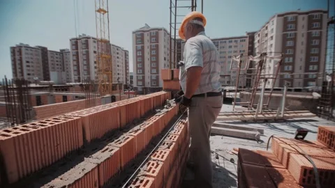 Elder builder man uses cement to concrete a red bricks wall Stock Footage 143787447