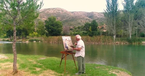 Elder picture painter working by a river in autumn Stock Footage 124382926