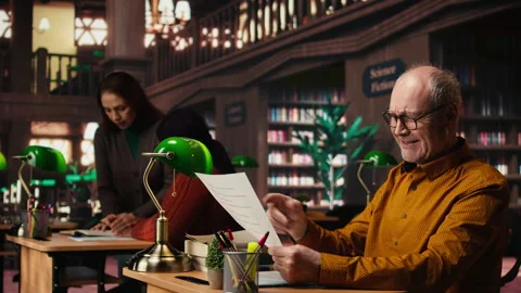 Elderly actor in a library focusing on script reading and memorization Stock Footage 313310457