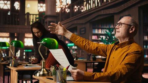 Elderly actor in a library focusing on script reading and memorization Stock Photos