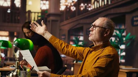 Elderly actor in a library focusing on script reading and memorization Stock Photos