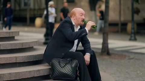 Elderly bald man drinking alcohol after work on stairs, struggling with life Stock Footage 318879581