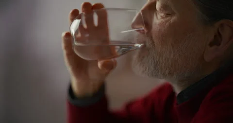 Elderly bearded man drinking water indoors in soft natural light Stock Footage 336288577