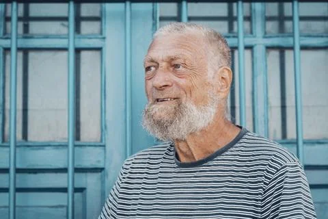 Elderly bearded man smiling in front of blue wooden window wearing striped .. Stock-Fotos