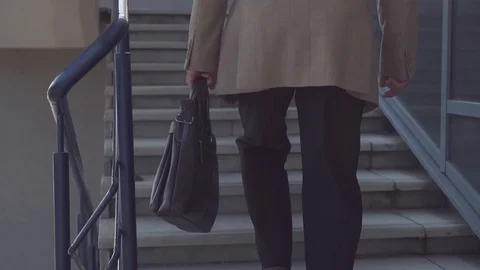 An elderly businessman in a jacket and tie with a briefcase climbs the stairs in Stock Footage 101510004