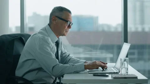 Elderly businessman look at phone and working with computer in modern office Stock Footage