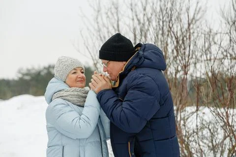 An elderly caring man warms his wife's hands with his breath on the street. Stock Photos