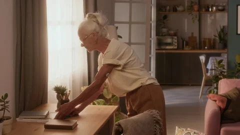 Elderly Caucasian Lady with Diabetes Patch Cleaning Up Dust on Table Stock Footage 320971592