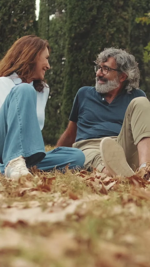 Elderly couple chatting while sitting on the grass in park, Camera moving Vidéo 254424987
