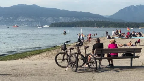Elderly Couple cyclists sit on bench with beach and mountain view Stock Footage 280806549