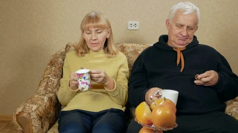 Elderly couple drink tea and eat sweets. Husband and wife sitting at home on the Stock Footage 71246952