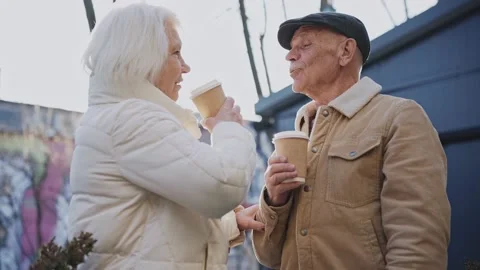 An elderly couple drinks from coffee cups on a sunny street, talking and smiling Video stock 178950423