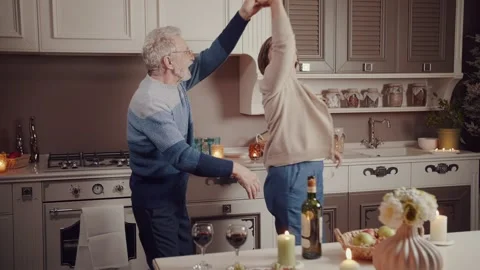 Elderly couple drinks wine, laughs, and dances in the evening in the kitchen Stock Footage 234990215
