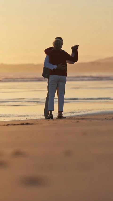 Elderly couple embracing and pointing at sunset on beach Stock Footage 327715437