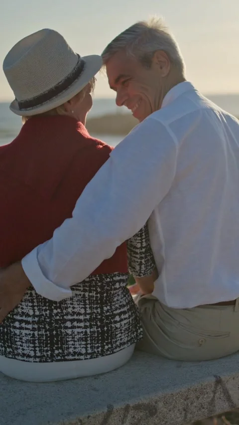 Elderly couple embracing on bench at sunset by the ocean Stock Footage 327714967