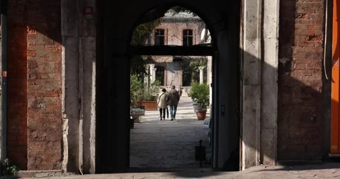 Elderly couple holding hands through a sunlit courtyard arch Stock Footage 320170673
