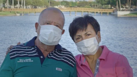 Elderly couple looking at camera while wearing face masks in front of a lake Stock Footage 126605464