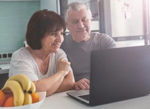 Elderly couple looking at computer in the kitchen Stock Photos