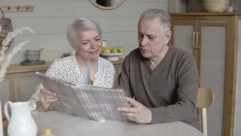 An elderly couple sits at a table looking at a photo album Stock Footage 172115571