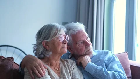 Elderly Couple Sits Thoughtfully on Sofa, Embracing and Looking Away Together	 Stock Footage 332684243