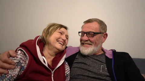 Elderly couple sitting on the couch embracing and smiling at each other. Happy Stock Footage 142807889