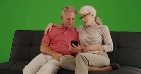 Elderly couple sitting on couch using smartphone on green screen Stock Footage