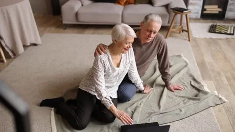 An elderly couple sitting on the floor in front of their laptop. Stock Footage 180439634