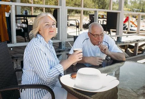 An elderly couple is sitting at a table in a cafe by the sea, looking at the  Stock Photos