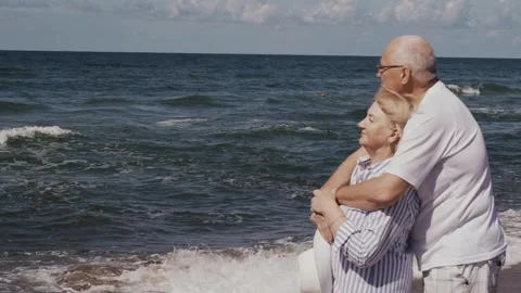 An elderly couple stand hugging on the beach by the sea, look at the waves Stock Footage 250558236