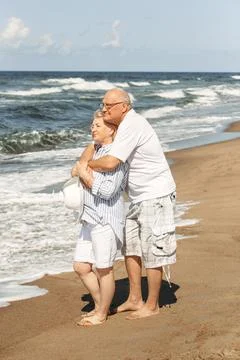 An elderly couple stand hugging on the beach by the sea, look at the waves,.. Stock Photos