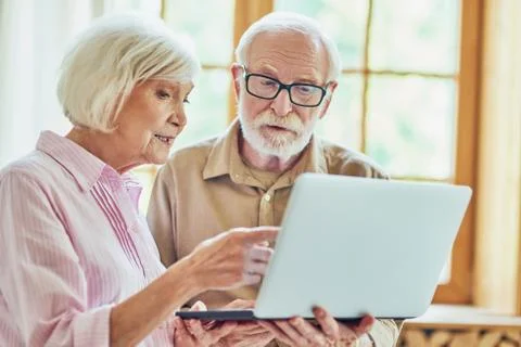 Elderly couple using computer near the window at their house Stock Photos
