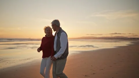 Elderly couple walking on the beach at sunset Stock Footage 310002283
