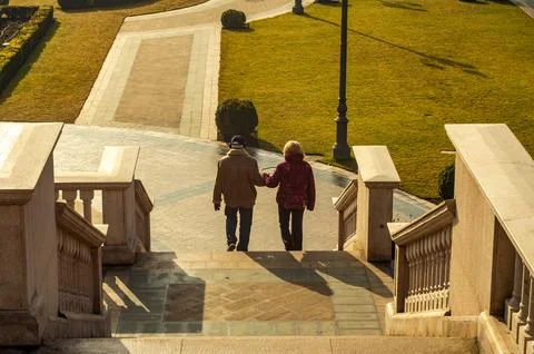 Elderly Couple Walking Down Stone Staircase in Sunlit Park Stock Photos