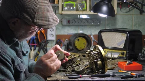 An elderly craftsman, in a workshop, repairs an old clock mechanism Stock Footage 294834991