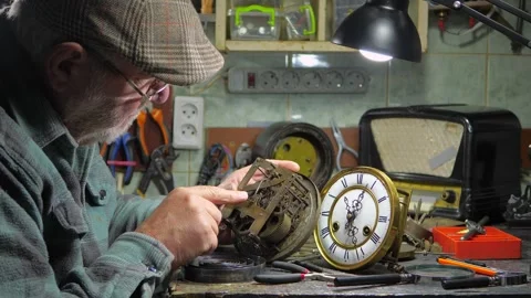 An elderly craftsman, in a workshop, repairs an old clock mechanism Stock Footage 294835025