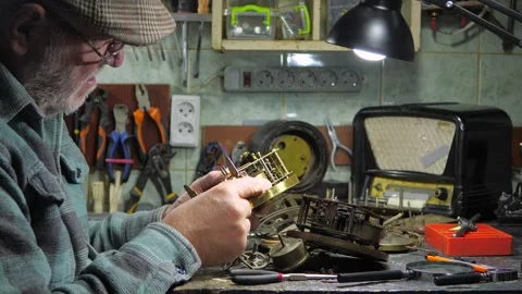 An elderly craftsman, in a workshop, repairs an old clock mechanism Stock Footage 294835068